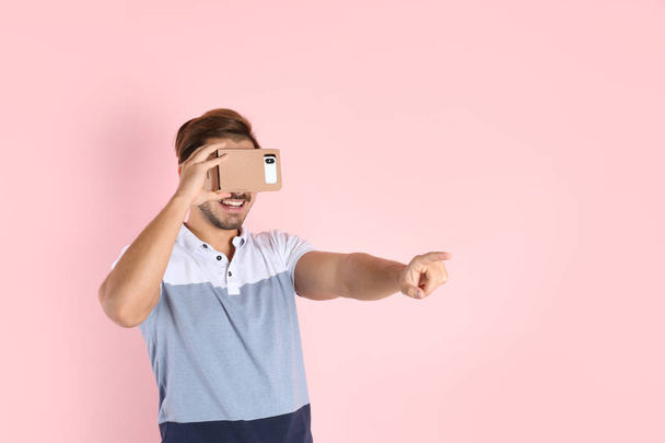 Young man using cardboard virtual reality headset on color background. Space for text - Foto, Bild