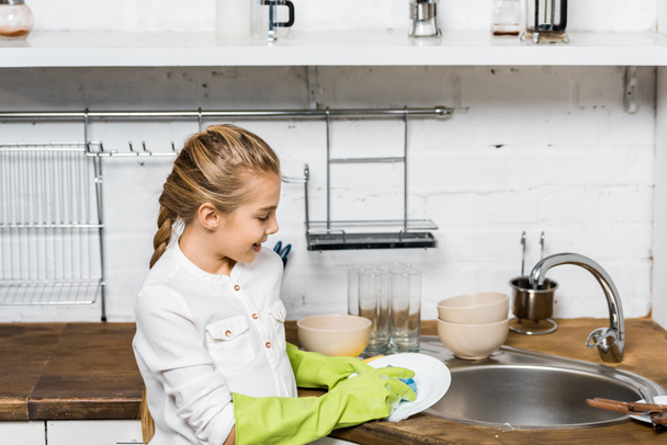 χαριτωμένο κορίτσι με λαστιχένια γάντια, Πλύσιμο πιάτων στην κουζίνα - Φωτογραφία, εικόνα