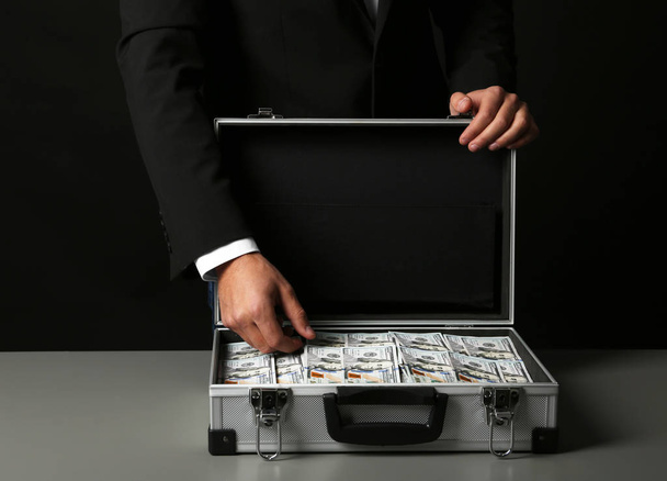Businessman with suitcase full of money on dark background - Valokuva, kuva