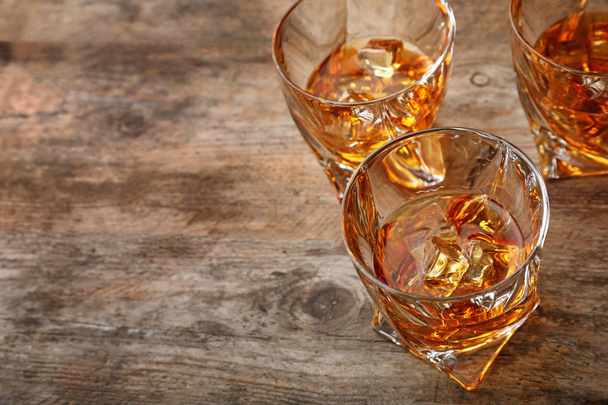 Golden whiskey in glasses with ice cubes on wooden table. Space for text - Fotografie, Obrázek