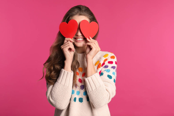 Portrait of young woman holding paper hearts near eyes on color background - Фото, зображення