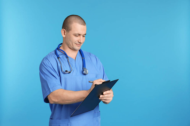 Portrait of medical assistant with stethoscope and clipboard on color background. Space for text - Foto, Imagen