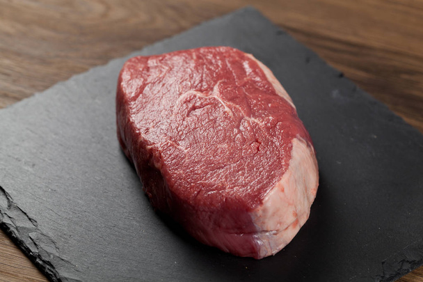 Raw beef steak on a dark wooden table. - Foto, Bild