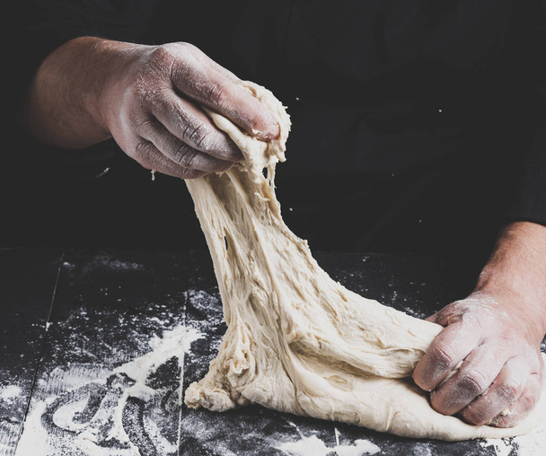 las manos masculinas sustituyen la masa de harina de trigo blanco sobre un fondo de madera negro, tonificación vintage
 - Foto, Imagen