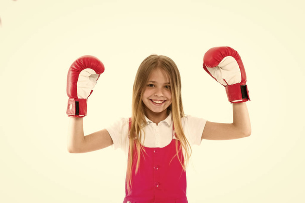 Enfance et garde d'enfants. L'athlète enfant montre sa puissance. Enfant heureux dans des gants de boxe isolés sur blanc. Petite fille sourire avant l'entraînement ou l'entraînement. Activité sportive et énergie
 - Photo, image
