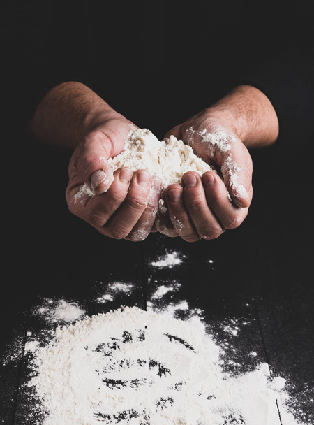 harina de trigo blanco en manos masculinas, fondo negro, tonificación vintage
 - Foto, Imagen