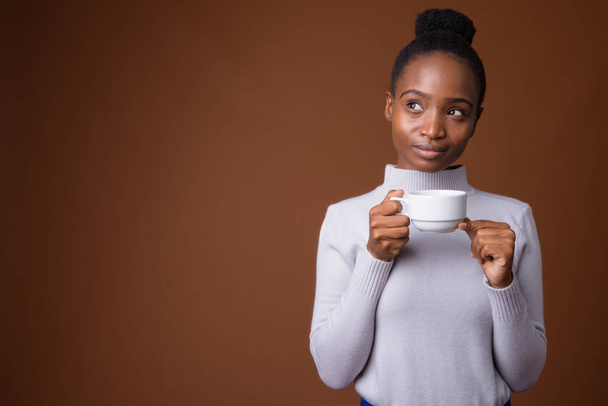 Young beautiful African Zulu woman holding coffee cup while thinking - Photo, Image