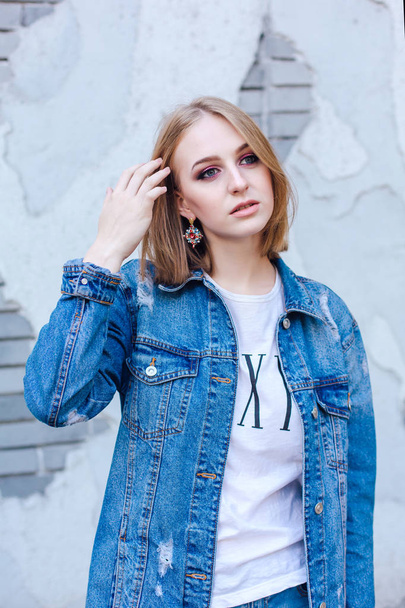 Fashion girl standing near brick wall in denim oversized jacket and beautiful ear rings. - Photo, image