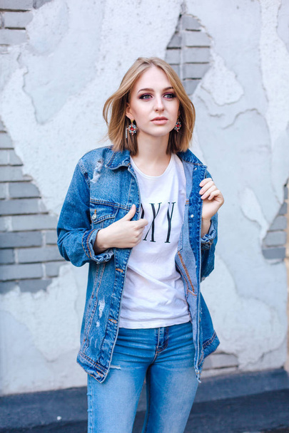 Fashion girl standing near brick wall in denim oversized jacket and beautiful ear rings. - Photo, Image