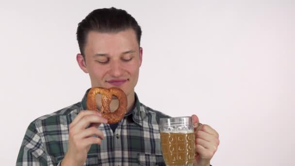 Young attractive man laughing joyfully, sipping delicious beer, holding a pretzel - Кадри, відео