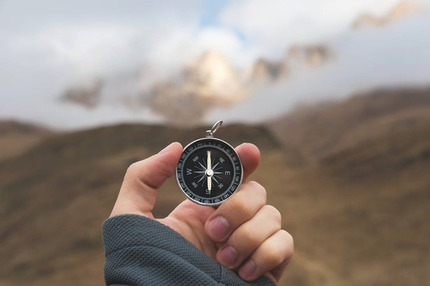 A male Hiker is looking for a direction with a magnetic compass in the mountains in the fall. Point of view shot. Mans hand with a watch bracelet holds a compass - 写真・画像