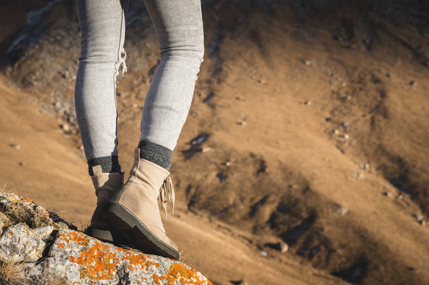 Close-up of female legs in stylish mountain boots standing on the top of a cliff on the background of a mountain slope - Photo, image