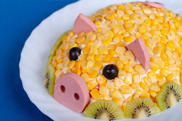 Maissalat im Stil des neuen Jahres - das Jahr des gelben Schweins. Symbol des neuen Jahres 2019 auf dem chinesischen Horoskop. Festmahl. Salat in Form eines niedlichen Schweins auf blauem Hintergrund. - Foto, Bild