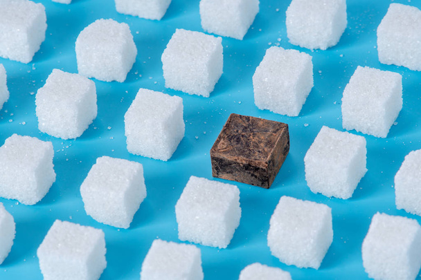 Pattern of sugar refined cubes and one chocolate blue background. The concept of harmful ingredient for confectionery - Photo, Image