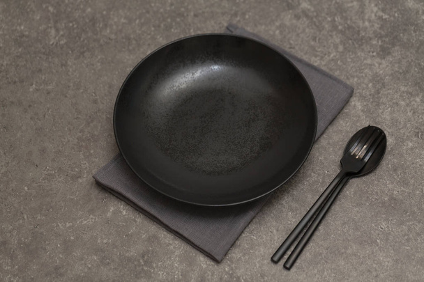 Black plate, Cutlery and napkin on grey stone table. Top view - Photo, image