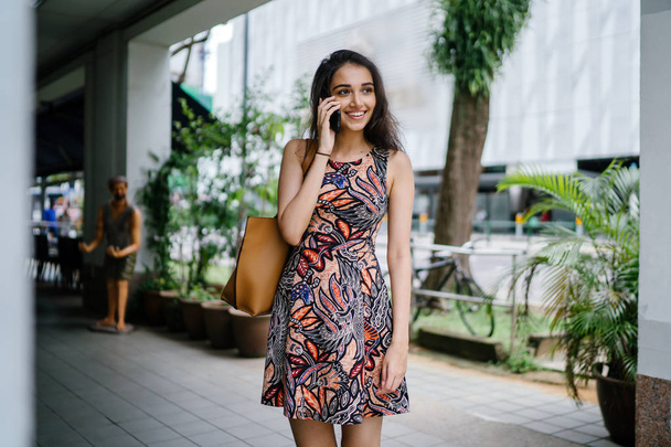 Young Indian Asian woman standing and talking on her smartphone on an urban street in a city in Asia during the day - Foto, Bild