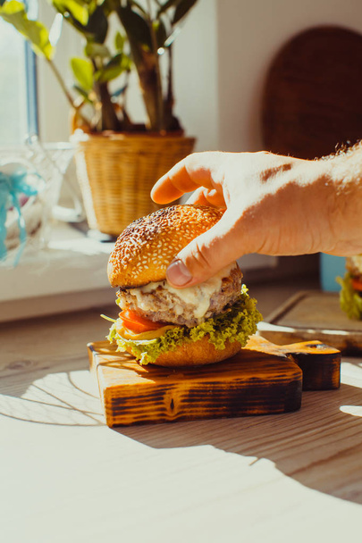 Man puts the bun on the beef burger on a rustic wooden board - Zdjęcie, obraz