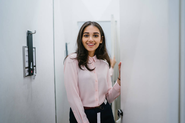 Portrait of a young and beautiful Indian Asian woman trying out new clothing in a fitting room in a fashion shop in a mall. - Foto, afbeelding