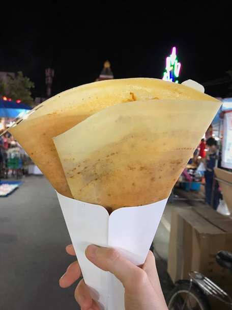 Una crepe appetitosa nella mano destra tra festa del tempio o fiera annuale. Concetto di street food
. - Foto, immagini