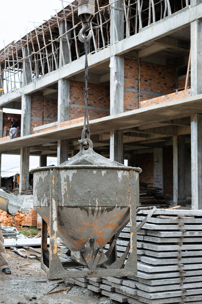 Macchinari gru sollevamento cemento malta miscelatore secchio contenitore davanti a un cantiere
 - Foto, immagini