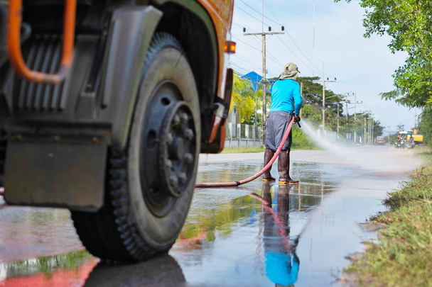 працівник розпилює воду, щоб очистити дорогу водою під тиском, мокрим прибиранням вулиці
. - Фото, зображення