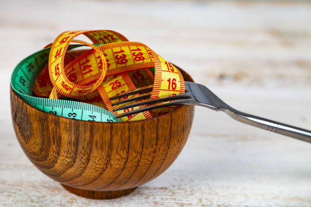Measuring tape in a wooden bowl and fork. Concept of diet and weight loss. - Zdjęcie, obraz