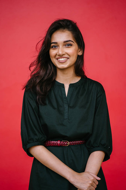 Studio portrait of a beautiful, young and attractive Indian Asian woman against a red studio background. She is elegantly dressed - Valokuva, kuva