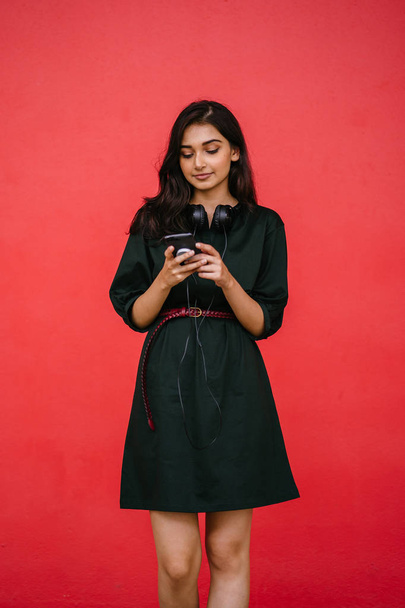 Young, attractive and beautiful Indian Asian millennial girl dancing as she listens to music on her headphones. She is streaming music on her smartphone - Foto, Bild