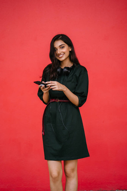 Young, attractive and beautiful Indian Asian millennial girl dancing as she listens to music on her headphones. She is streaming music on her smartphone - Photo, image