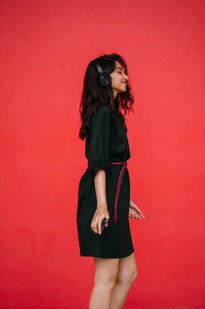 Young, attractive and beautiful Indian Asian millennial girl dancing as she listens to music on her headphones. She is streaming music on her smartphone - Fotó, kép