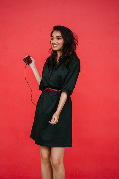 Young, attractive and beautiful Indian Asian millennial girl dancing as she listens to music on her headphones. She is streaming music on her smartphone - Foto, afbeelding