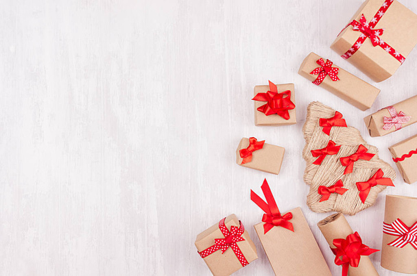 Christmas festive background - different gifts boxes of kraft paper and red ribbons, bows as border on soft white wood board. - Foto, afbeelding