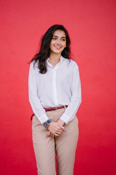 Studio portrait of a beautiful, young and attractive Indian Asian woman against a red studio background. She is elegantly dressed - Foto, immagini