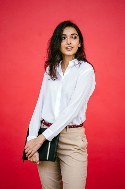 Studio portrait of a beautiful, young and attractive Indian Asian woman against a red studio background. She is elegantly dressed - Фото, зображення