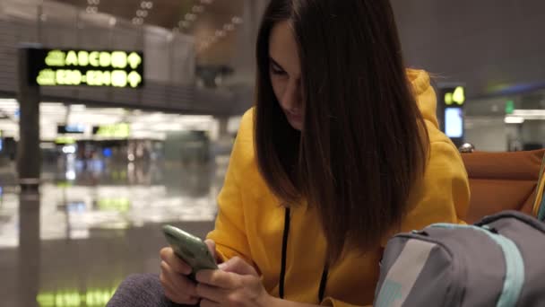 Молода жінка використовує смартфон у залі очікування в аеропорту
 - Кадри, відео