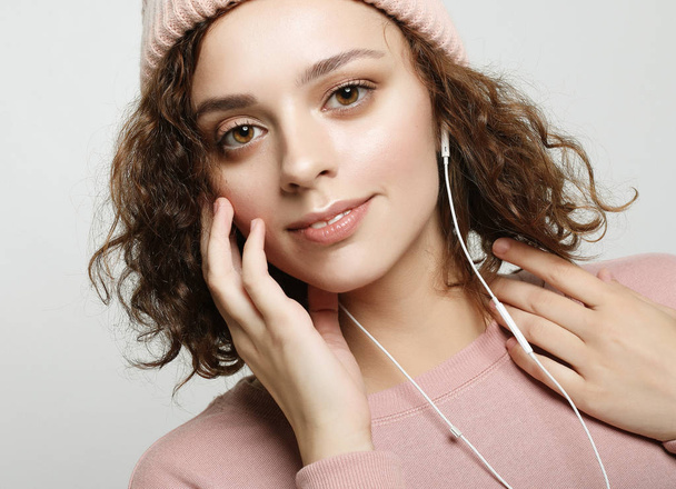 beautiful girl in headphones listens to music and smiles while standing on a white background in a pink sweatshirt and hat. - Fotó, kép