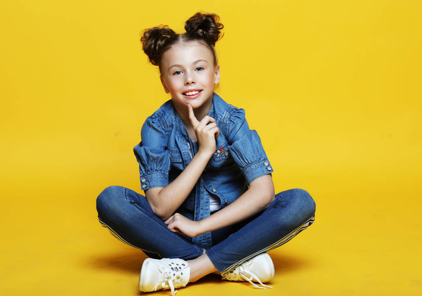 cute little girl sitting and smiling, isolated on yellow background - Фото, зображення