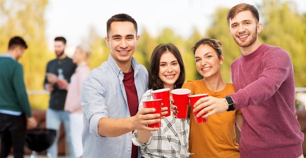 celebration, friendship and people concept - group of smiling friends toasting non alcoholic drinks in party cups over rooftop party background - Фото, зображення