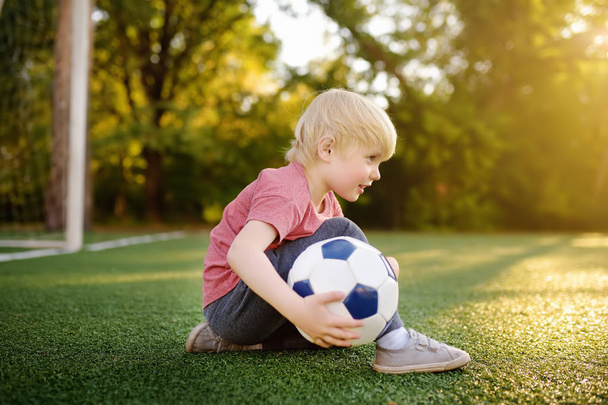 Little boy having fun playing a soccer/football game on summer day. Active outdoors game/sport for children. Kids soccer classes and camps - Photo, Image