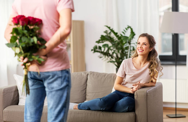woman looking at man with bunch of flowers at home - Fotoğraf, Görsel