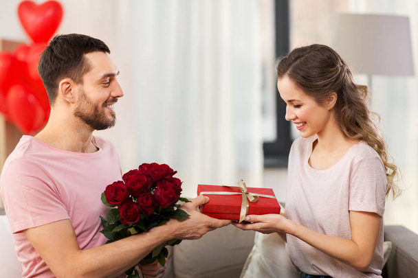 happy man giving woman flowers and present at home - 写真・画像