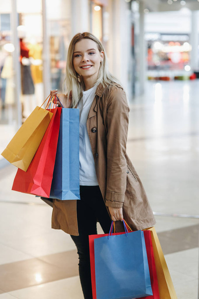 Blond girl smile and hold in her hands cool shooping bags different colour - red , blue, yellow. Concept: shopping, sales, Consumerism, lifestyle - 写真・画像