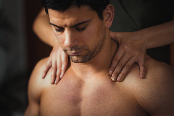 Physiotherapist massaging male patient with injured neck muscle. Sports injury treatment - Foto, Imagen