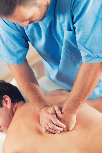 Physiotherapist doing healing treatment on man's back. Therapist wearing blue uniform. Osteopathy. Chiropractic adjustment, patient lying on massage table - Fotografie, Obrázek