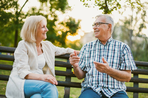 Два счастливых пожилых человека сидят и разговаривают в парке
.  - Фото, изображение