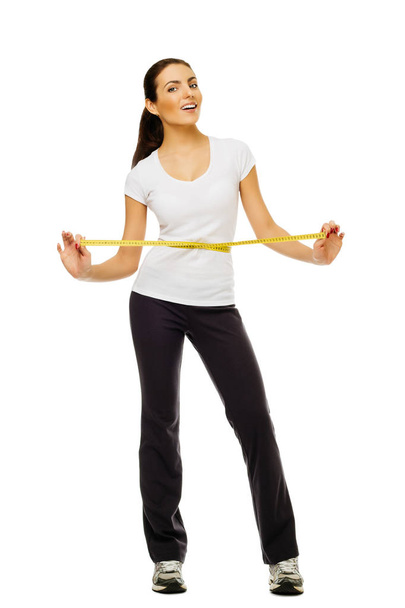 Young woman measuring her waistline with a measuring tape over white background. - Foto, imagen