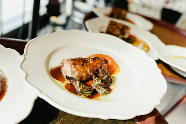 Muchos platos lomo de cerdo confitado con alcachofas y jugosa salsa servida por los camareros en un restaurante de lujo. - Foto, Imagen