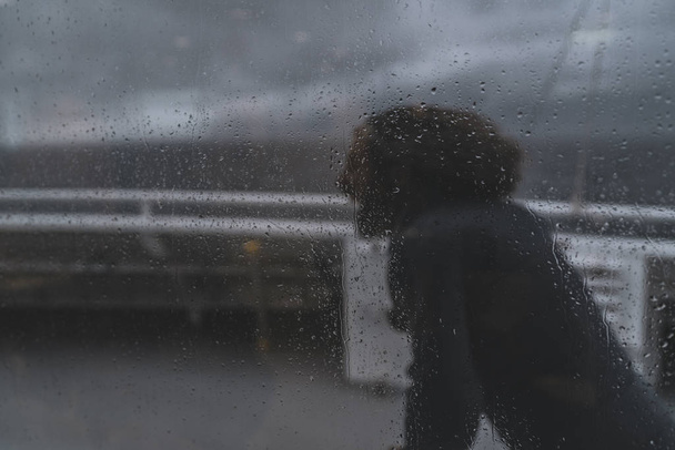 Μακρυμάλλης άνθρωπος περπάτημα προσήνεμα ιδωμένη μέσα από ανεμοθύελλα μια βάρκα σε μια βροχερή μέρα. - Φωτογραφία, εικόνα