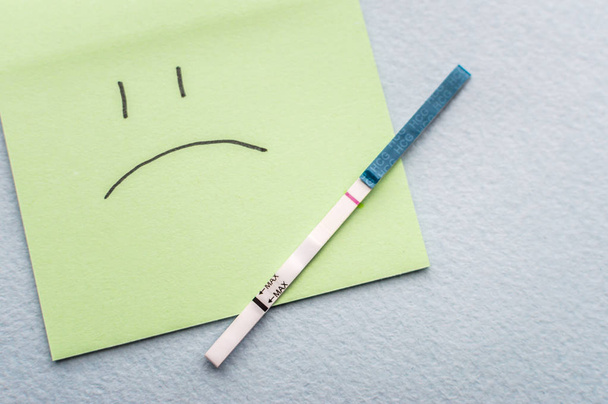 One-strip pregnancy test and sad smile. Infertility concept - Фото, изображение