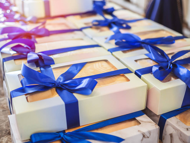 Білі сувенірні подарункові коробки з блакитними стрічками для гостя, який відвідує весілля
. - Фото, зображення